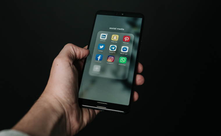 A hand holding a smartphone. The phone's screen displays various social. media icons.