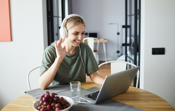 Woman wearing headphones and waving at her open laptop