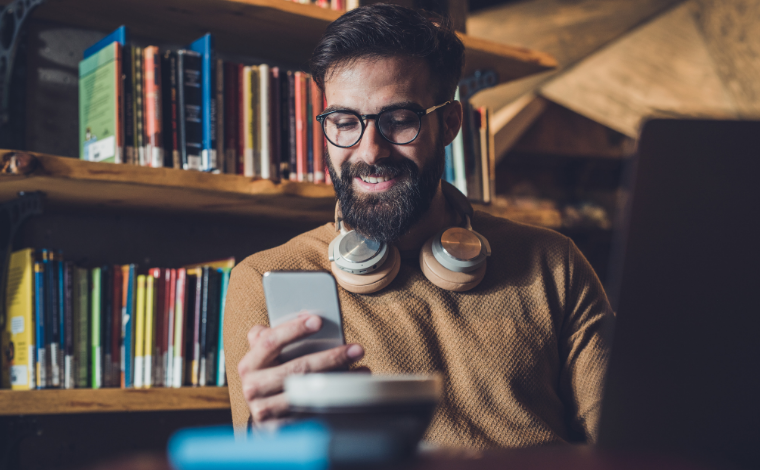 Person looking at their phone in a library and smiling