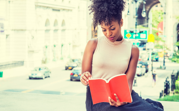 A person sitting and reading outside with a cityscape behind them