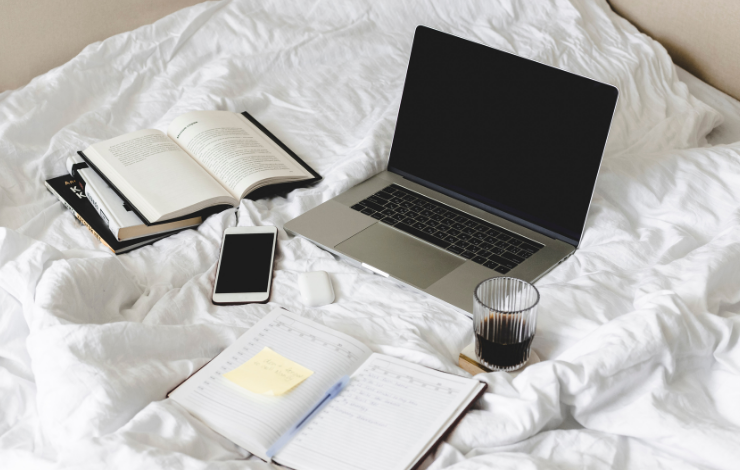 A laptop and open books on white bedding