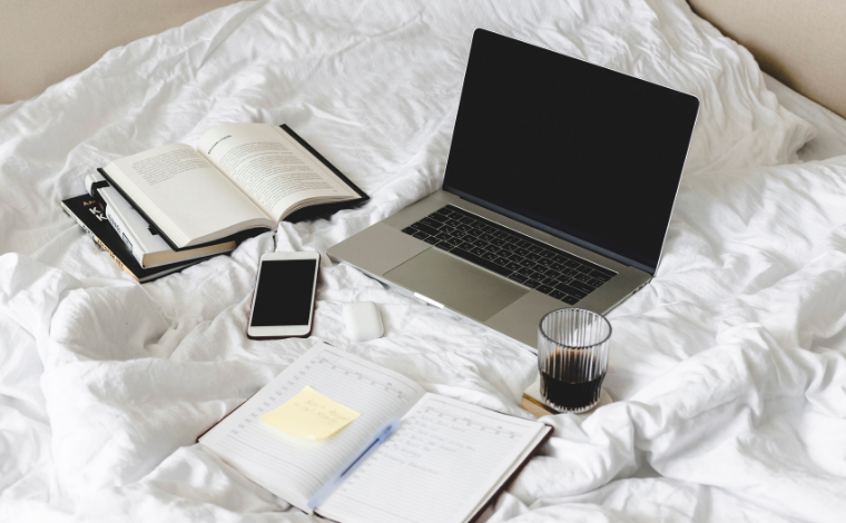 A laptop and open books on white bedding