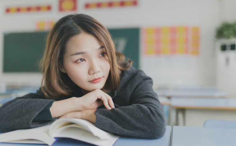 Person resting their arms on an open book and looking wistfully away