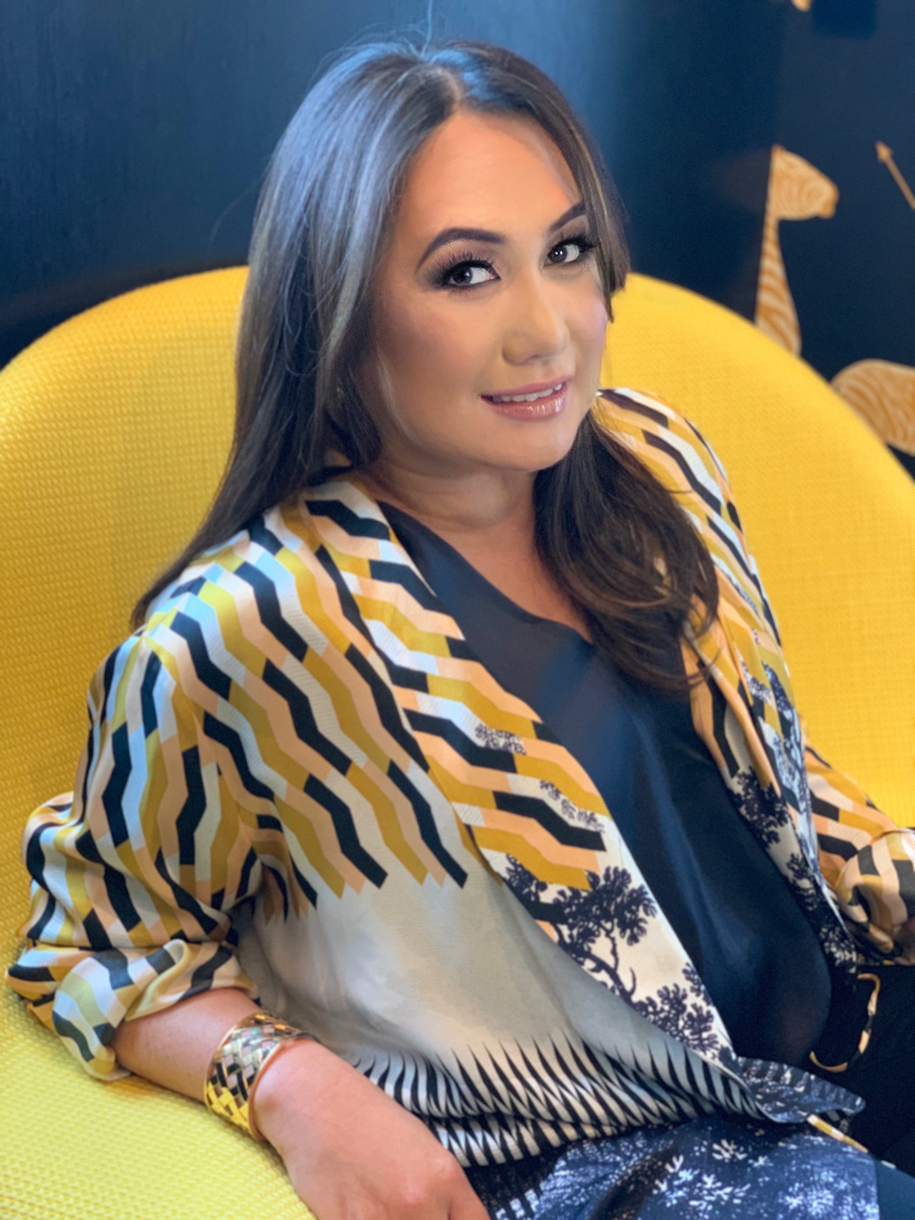 Melissa de la Cruz smiling and sitting in a yellow chair