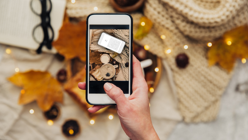 A hand holding a phone showing an open photography app above a flatlay