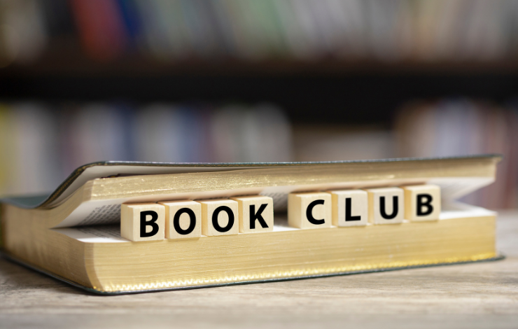 A book on its side with scrabble letters spelling out 'book club' sticking out from the pages
