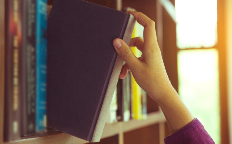 A hand pulling a book off a shelf