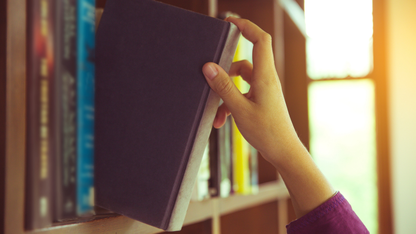 A hand pulling a book off a shelf