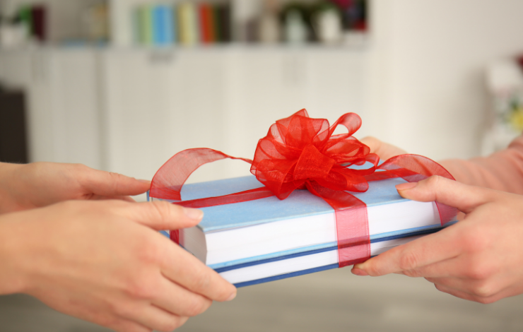 Two sets of hands exchanging books wrapped with a bow