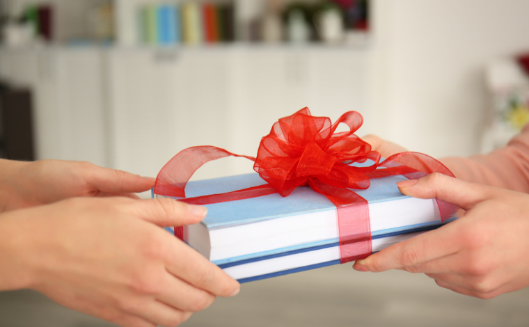 Two sets of hands exchanging books wrapped with a bow