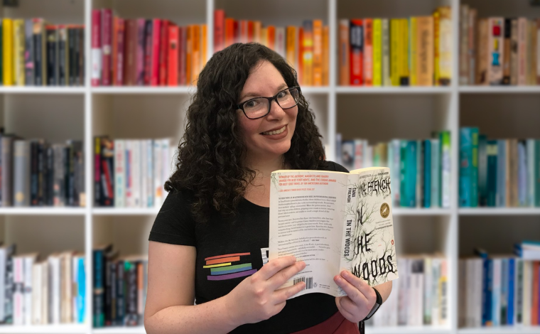 Kelly holding up a book in front of a bookshelf backdrop