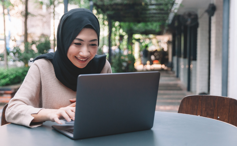 A person sitting outside and smiling at an open laptop