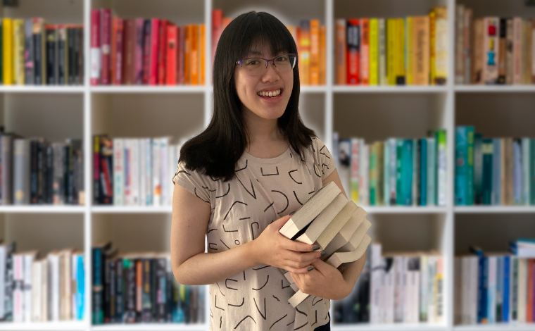 Emily holding a stack of books in front of a colorful bookcase
