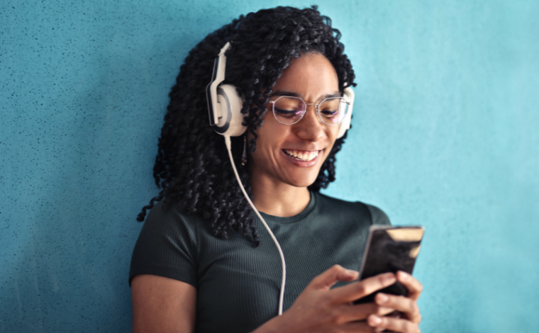 A person wearing headphones and grinning at their phone