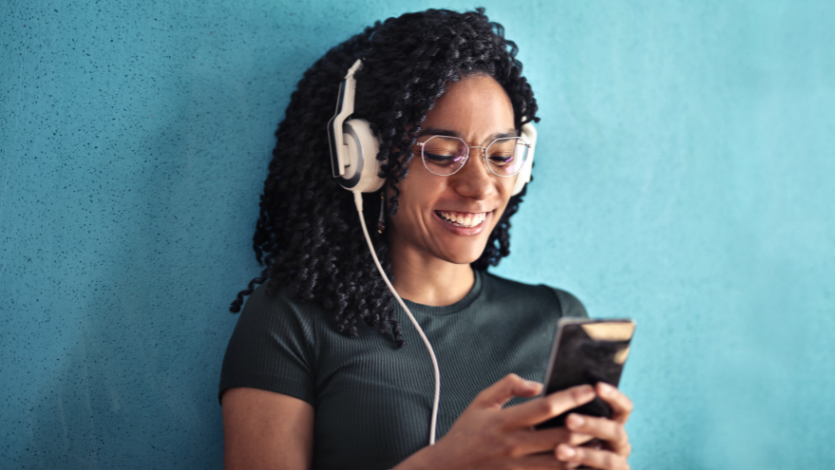 A person wearing headphones and grinning at their phone