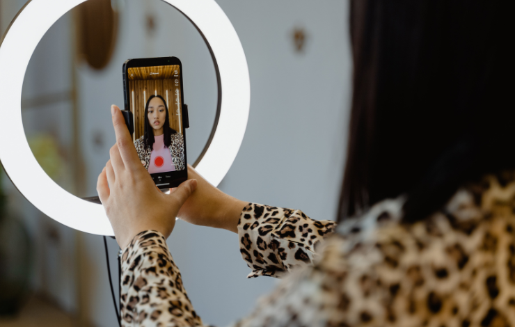 A person holding a phone in front of a ring light with the phone open to record a video