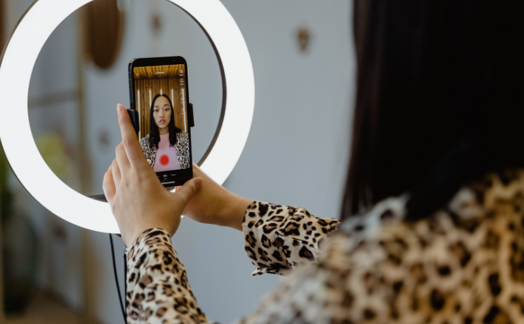 A person holding a phone in front of a ring light with the phone open to record a video