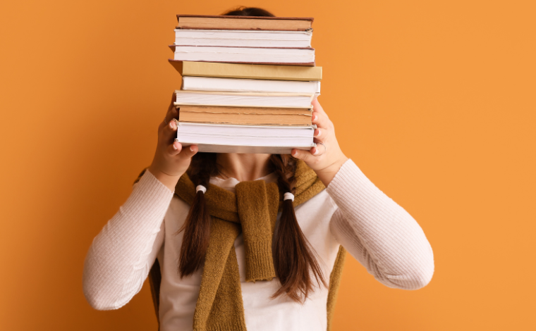 A person holding up a book stack in front of their face