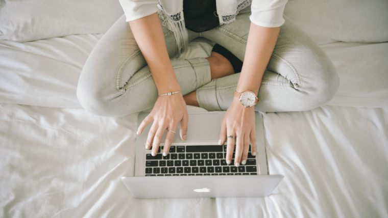 A view from above of someone sitting cross-legged on a bed typing on a laptop