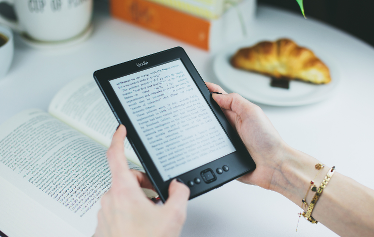 A white hand holding an e-reader in front of an open book
