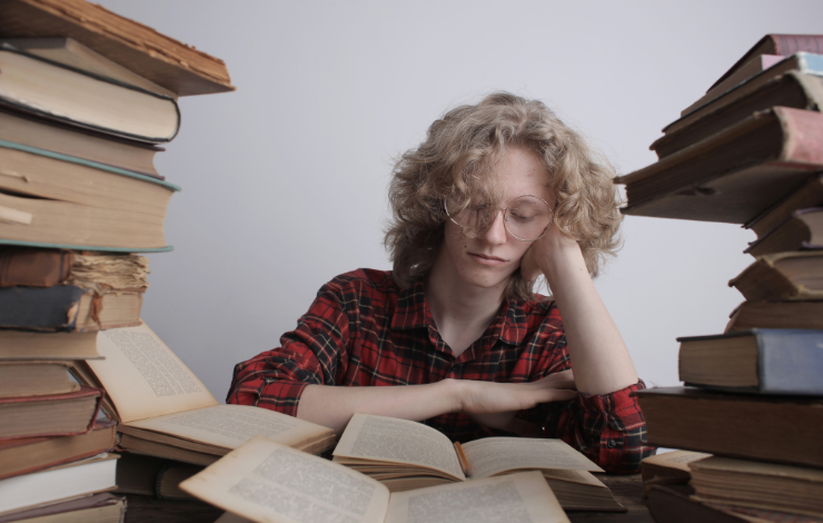 Person sitting surrounded by books and looking bored