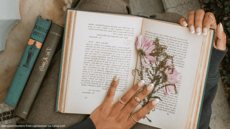 A brown hand with rings resting on an open book with pressed flowers inside
