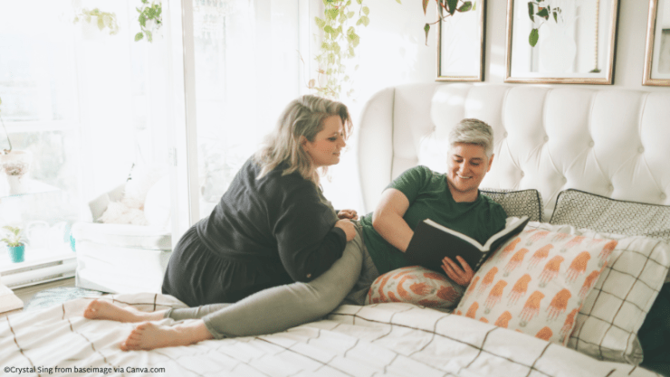 Two femme presenting people lying on a bed together and looking at a book