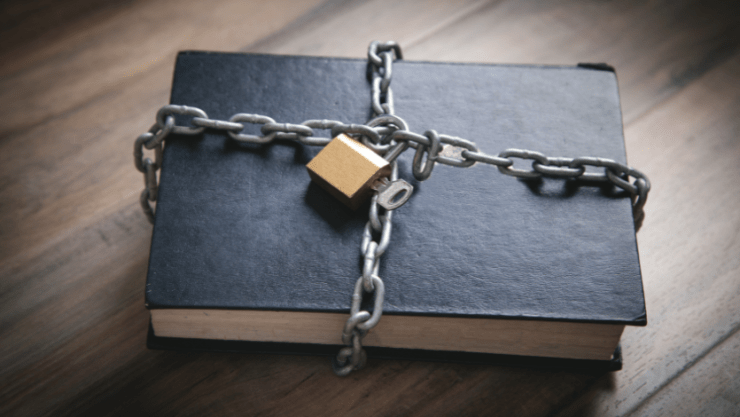 A black book covered in chains locked with a gold lock with a key inside