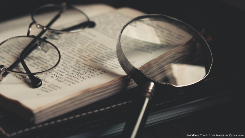 A magnifying glass on an open book beside glasses
