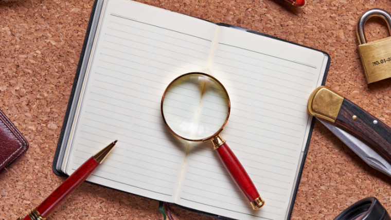A flatlay of an open notebook with a pen and magnifying glass on top