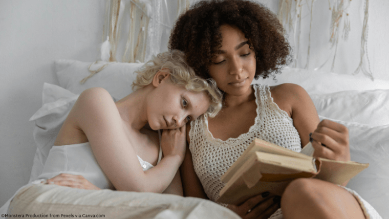 Two femme presenting people cuddled up reading a book together