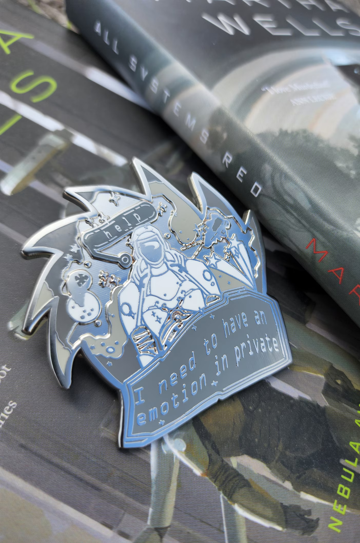 A silver pin featuring the character Murderbot