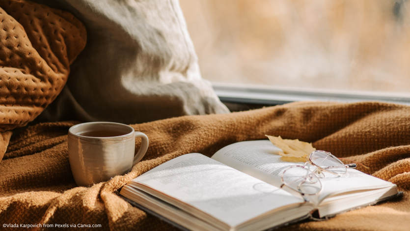 An open book sitting on top of a brown blanket in front of a window