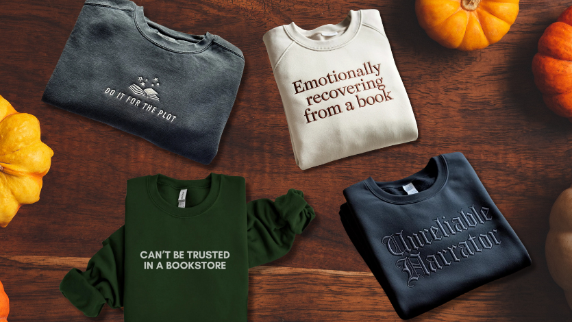 Four bookish sweatshirts on a flatlay of brown wood