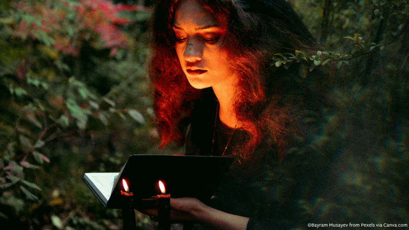 A girl in the forest with an open book in front of two candles